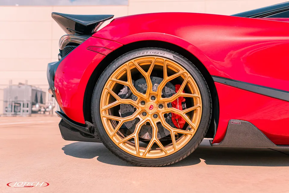 Close-up of a red McLaren's rear wheel, featuring gold multi-spoke wheels, red McLaren brake calipers, and carbon ceramic rotors.
