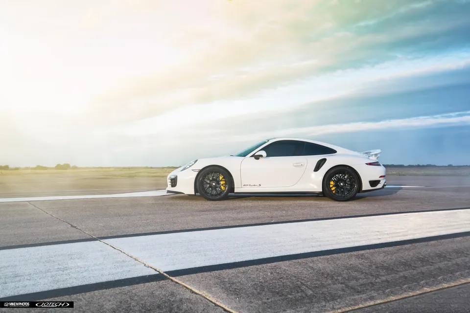 White Porsche 911 Turbo S parked on an airfield runway under a bright sky, showcasing its sleek design.