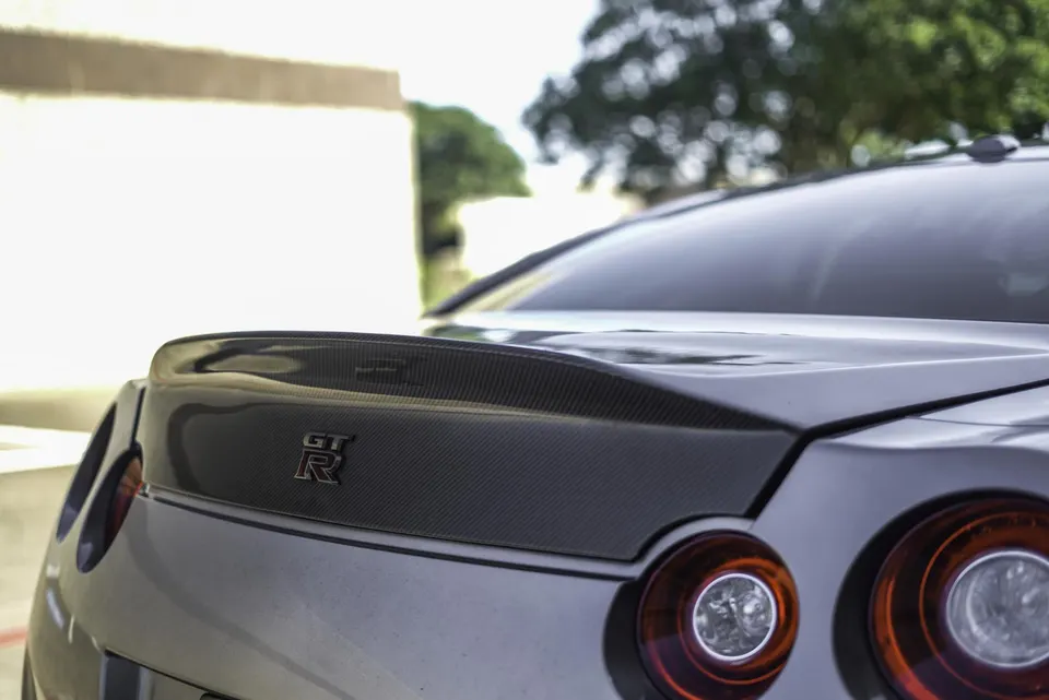 Close-up of the rear of a Nissan GT-R, showcasing a carbon fiber trunk lid with an integrated spoiler and round taillights.