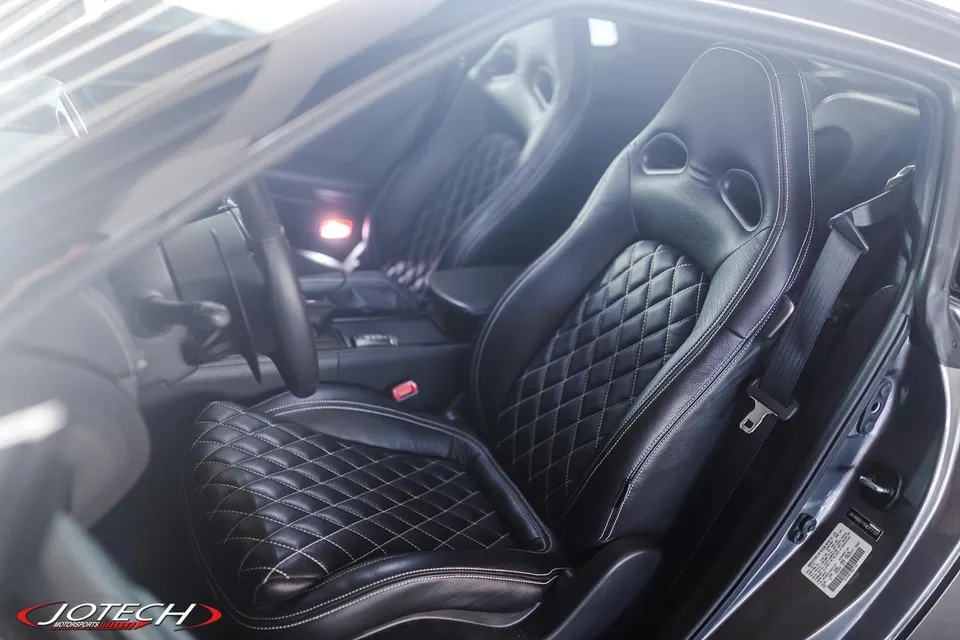 Close-up of a Nissan GT-R interior featuring custom black leather seats with white quilted stitching and a steering wheel.