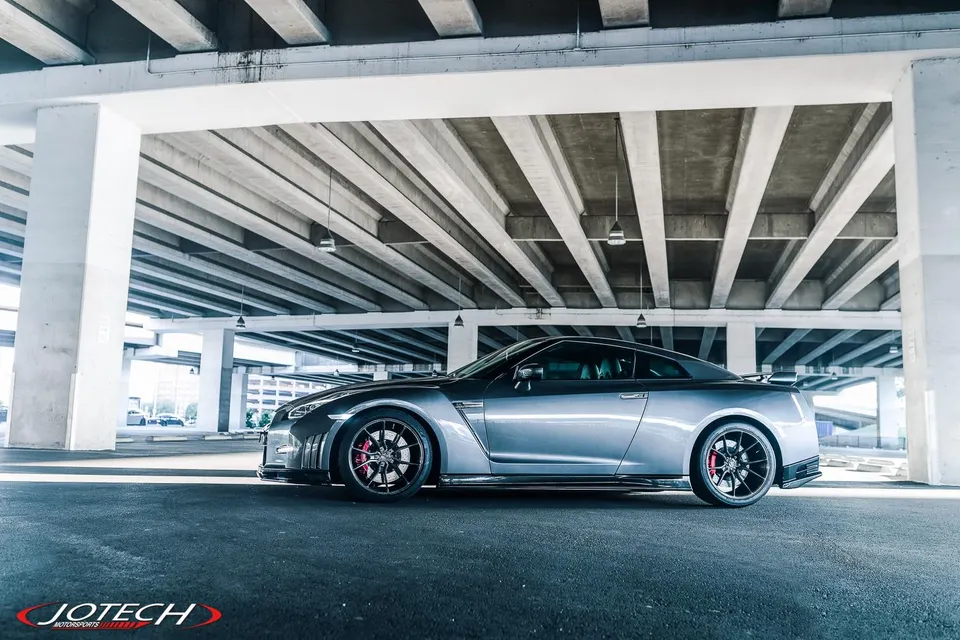 Grey Nissan GT-R R35 with aftermarket wheels and red brake calipers parked under a concrete overpass.