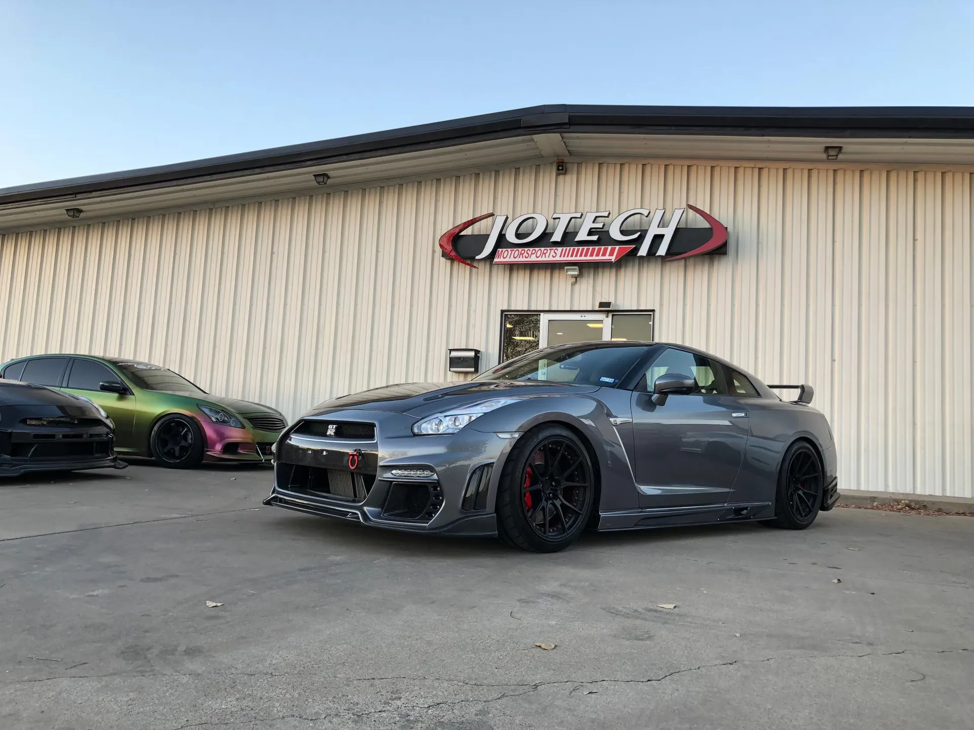 A gray Nissan GT-R and other modified cars parked outside Jotech Motorsports performance tuning shop.