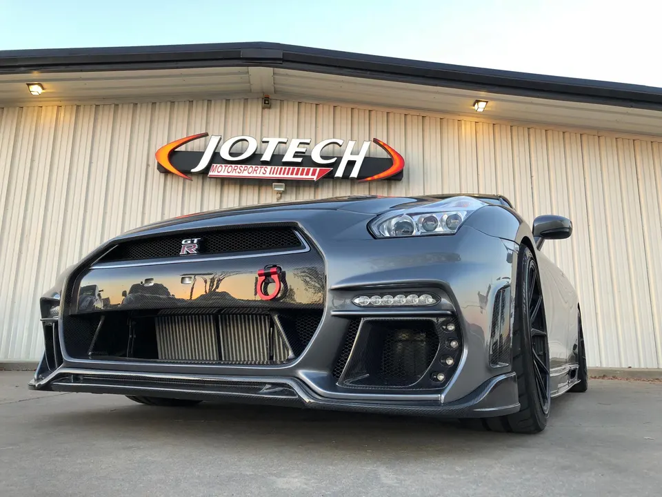Grey Nissan GT-R with carbon fiber front bumper and visible intercooler parked in front of Jotech Motorsports shop.