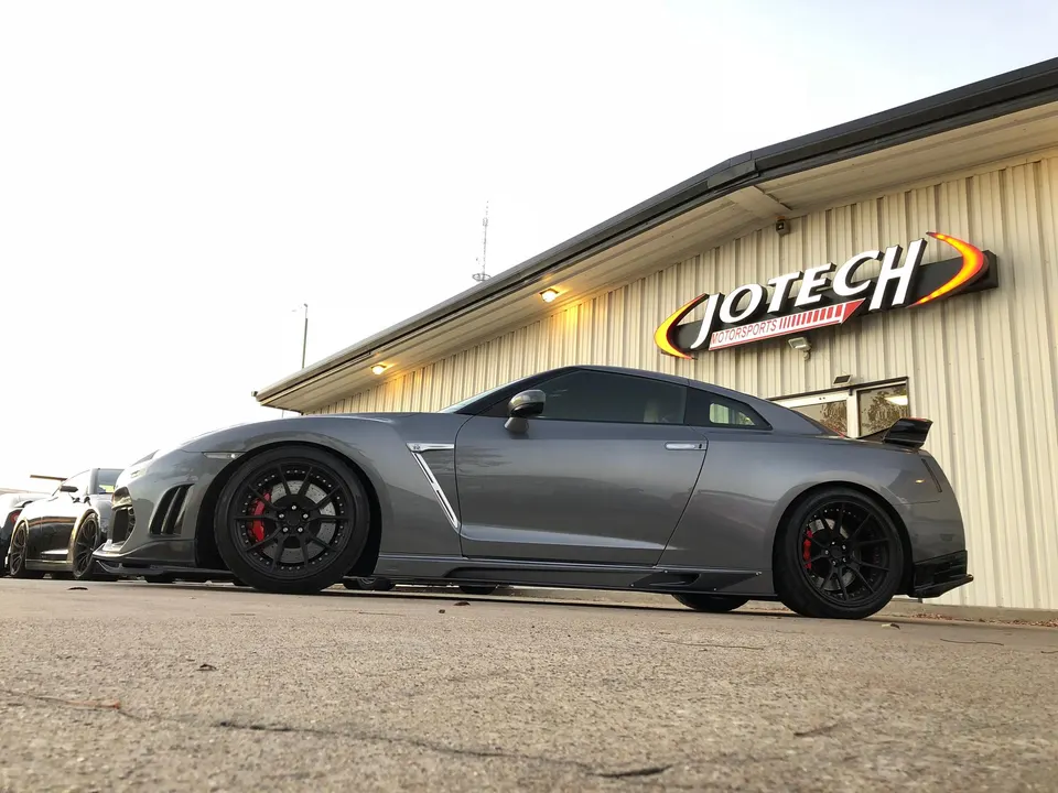 A grey Nissan GT-R R35 with custom wheels and aero parked outside Jotech Motorsports performance shop.