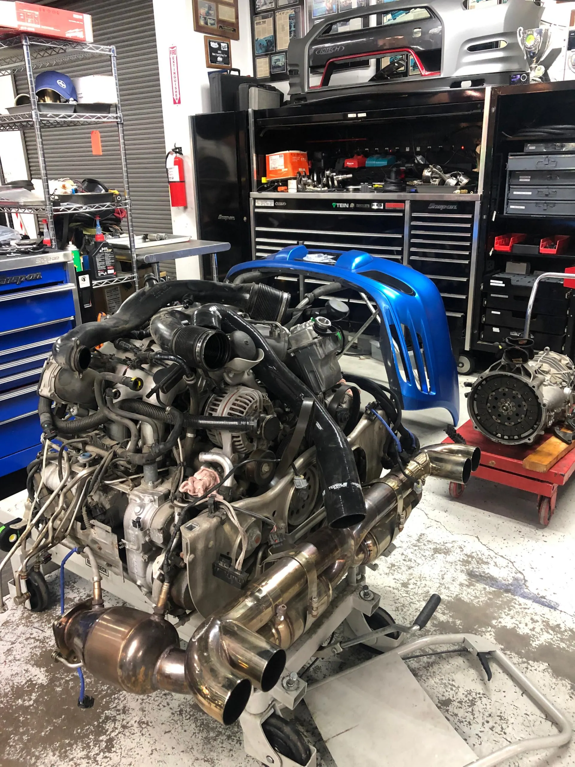 Engine and performance exhaust system on a stand in a Jotech Motorsports tuning shop.
