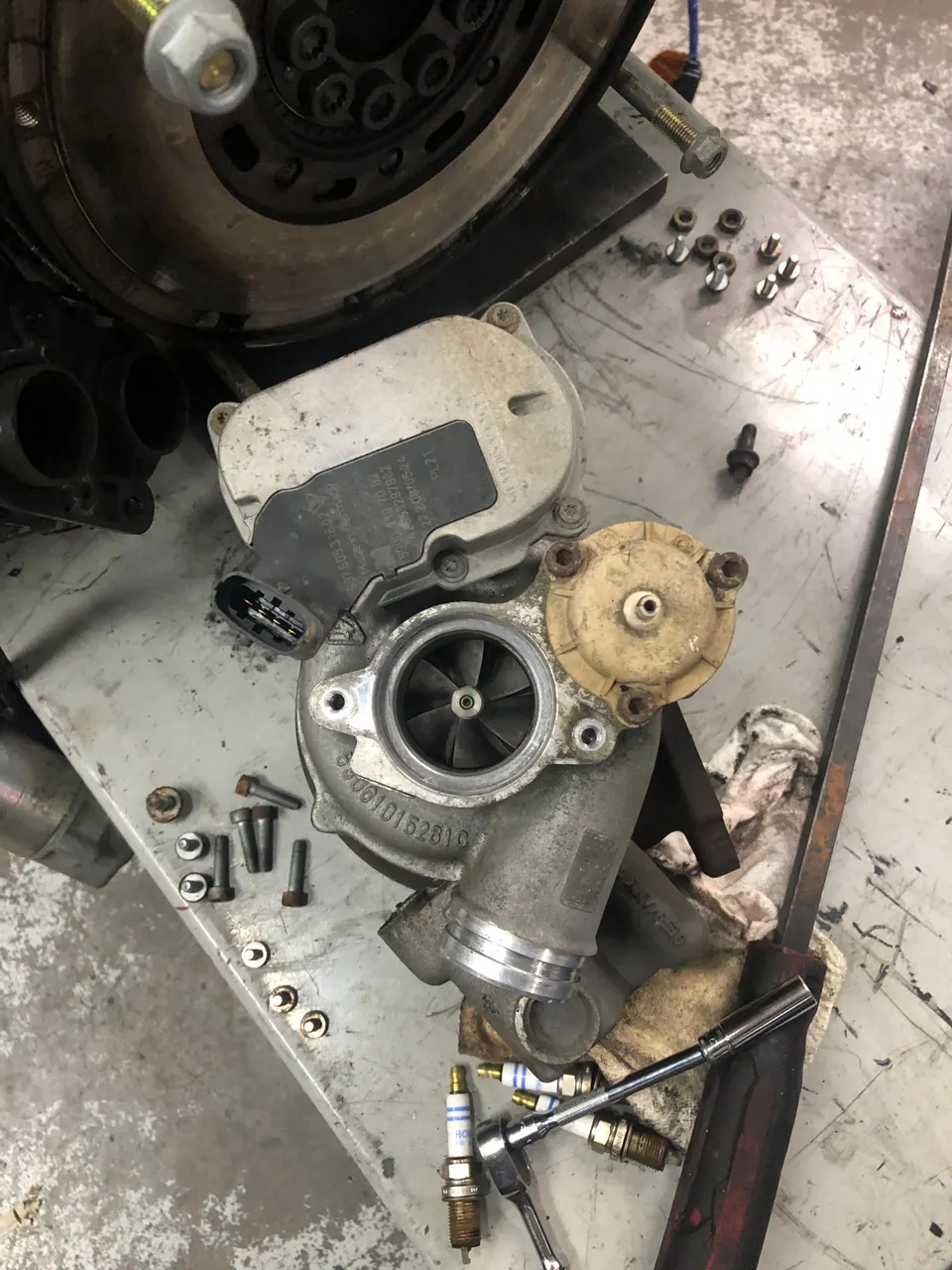 A turbocharger, spark plugs, and various engine components laid out on a workbench in a performance tuning shop.