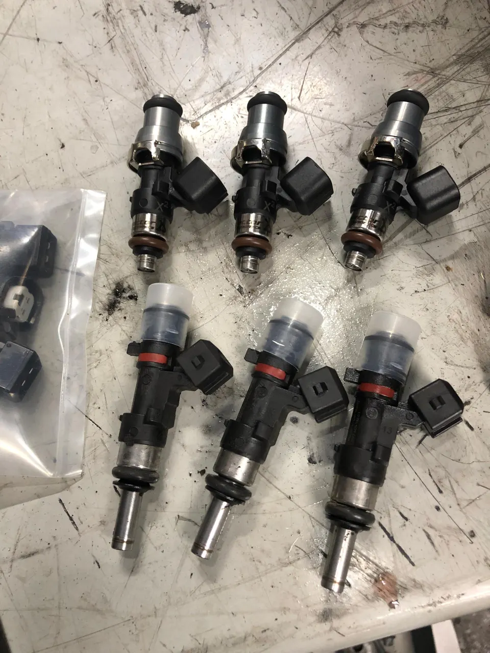 Six performance fuel injectors laid out on a workbench in a tuning shop, ready for installation.
