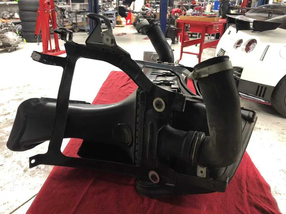 Nissan GT-R air intake system on a red cloth in a performance tuning shop with a white GT-R in the background.