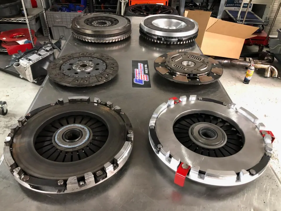 Multiple performance clutches and flywheels laid out on a metal workbench in a tuning shop.