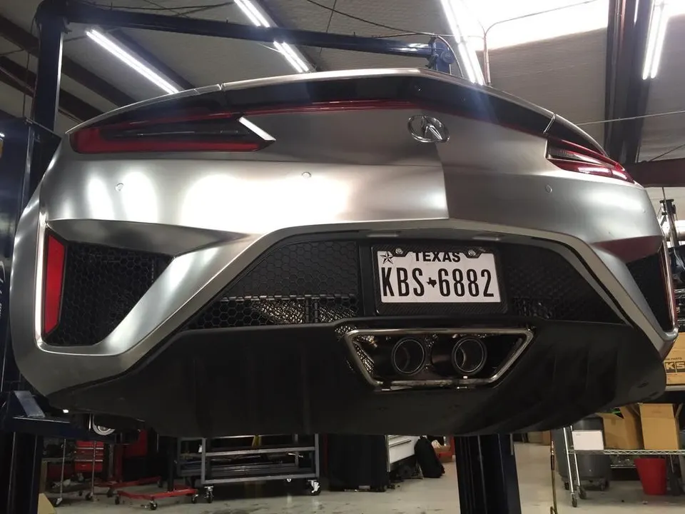 Rear view of a silver Acura NSX on a lift in a performance shop, showcasing its custom exhaust system.