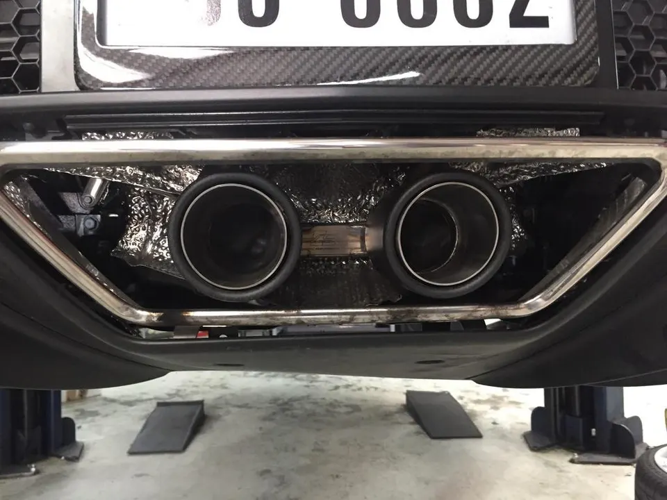 Close-up of a car's dual exhaust tips and heat shielding, with the vehicle on a lift in a shop.