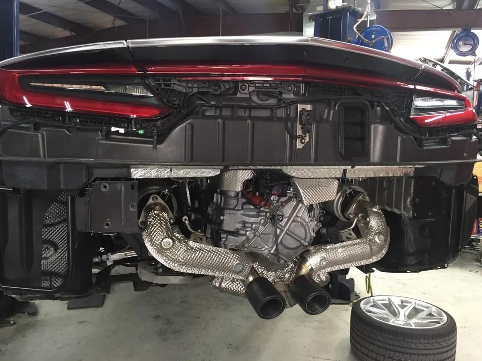 A Porsche 911 with its rear bumper removed, showcasing the exhaust system and engine in a performance shop.