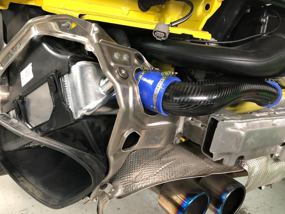 Aftermarket intercooler and carbon fiber intake pipe being installed in a yellow sports car.