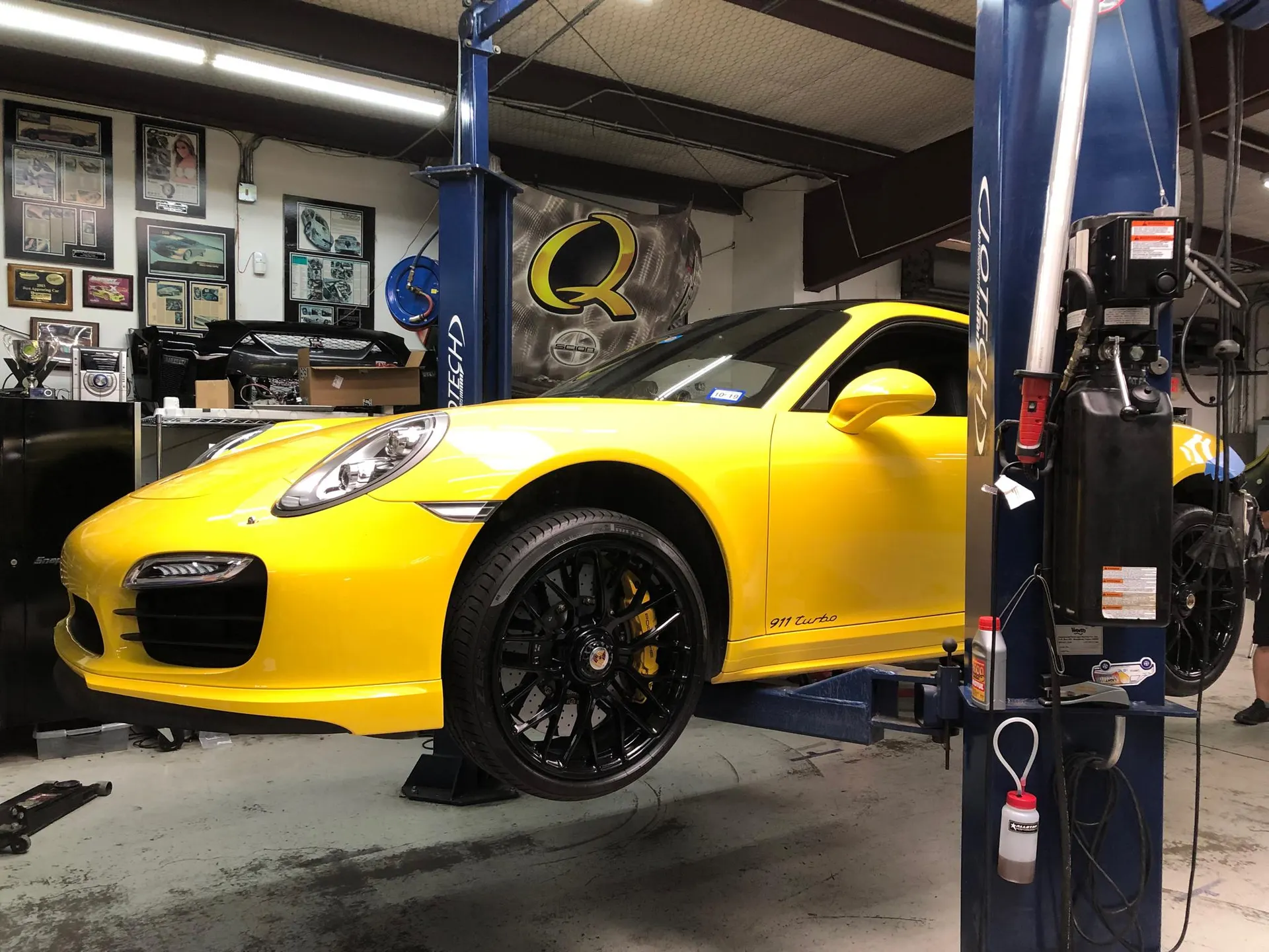 Yellow Porsche 911 Turbo on a hydraulic lift in a performance tuning shop, ready for service or modifications.