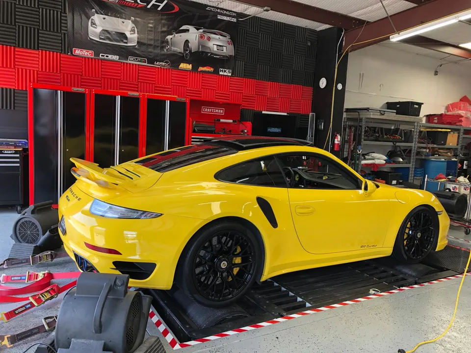 A bright yellow Porsche 911 Turbo strapped to a dynamometer in a performance tuning shop.