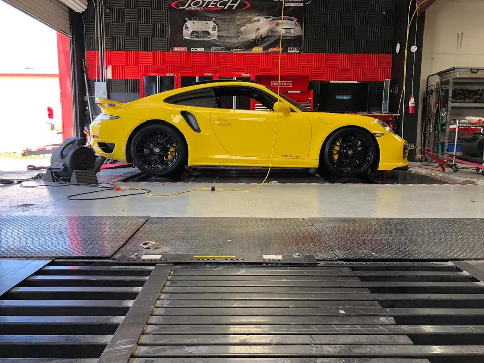 A bright yellow Porsche 911 Turbo strapped to a dynamometer at Jotech Motorsports for performance tuning.
