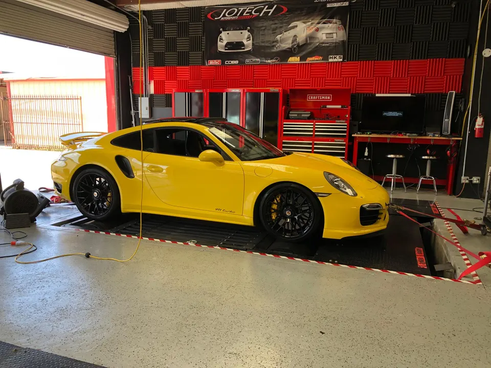 A bright yellow Porsche 911 Turbo strapped to a dynamometer at Jotech Motorsports, ready for performance tuning.