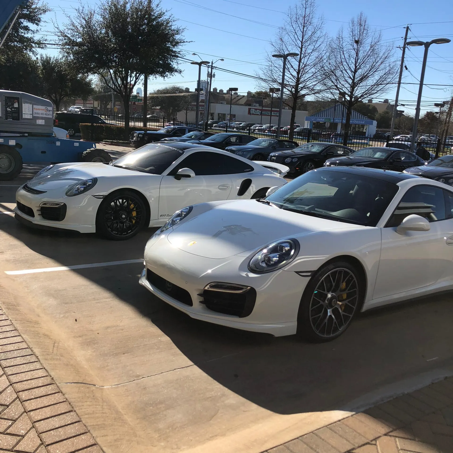 Two white Porsche 911 sports cars parked outdoors in a sunny parking lot, showcasing their sleek design.