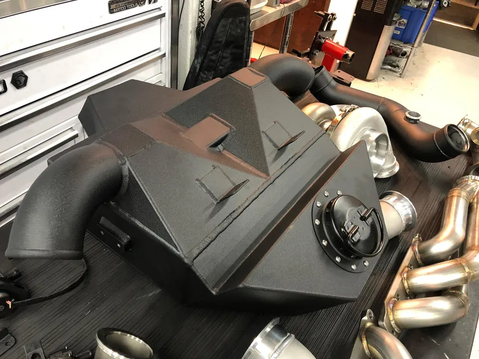 Performance engine parts including turbochargers, intercooler, and exhaust headers laid out on a workbench.