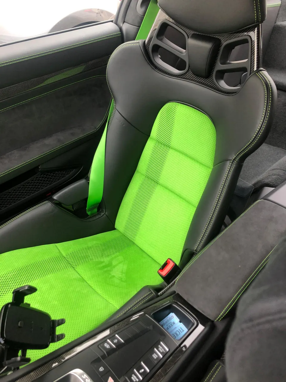 Close-up of a Porsche interior featuring a black sport seat with vibrant green accents, stitching, and seatbelt.