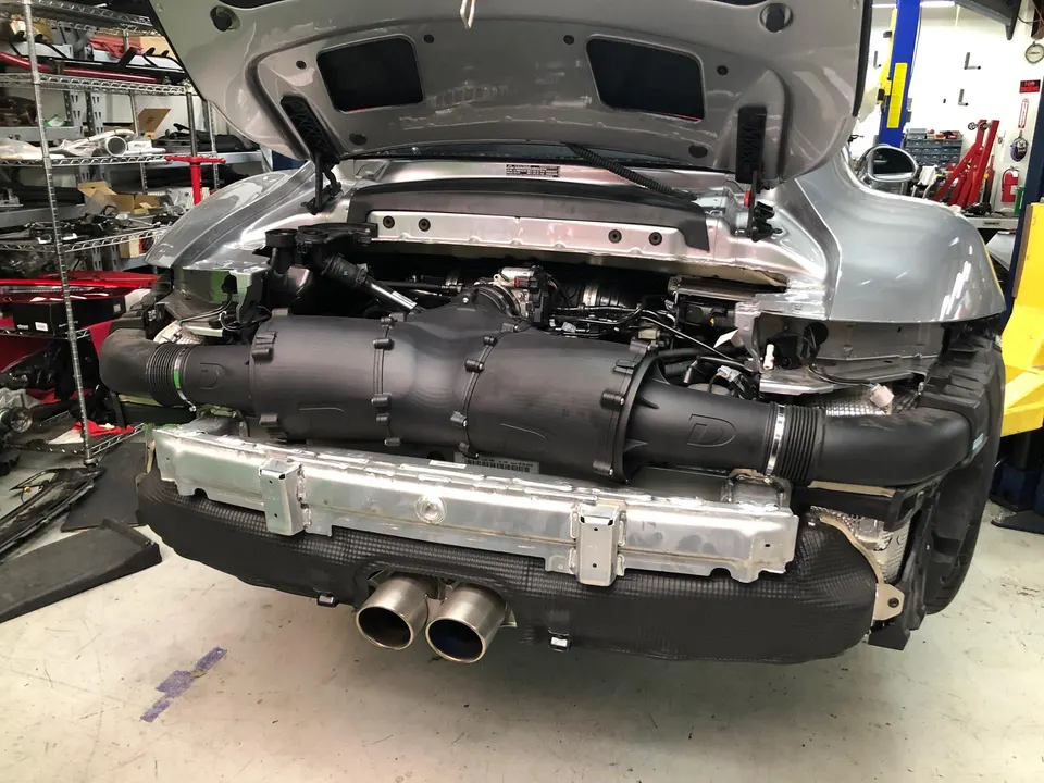 Porsche 911 with rear bumper removed, showcasing the engine bay, induction system, and exhaust tips in a performance shop.