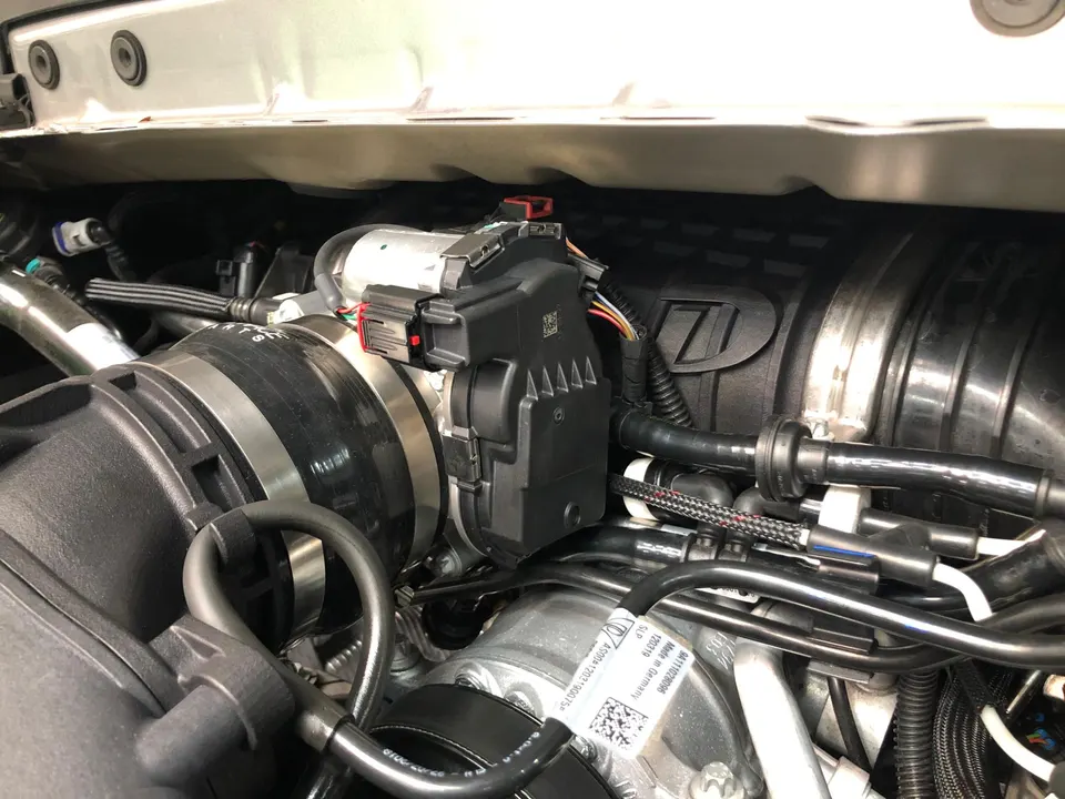 A close-up view of a car's engine bay, showing the throttle body and intake system with various hoses and wiring.