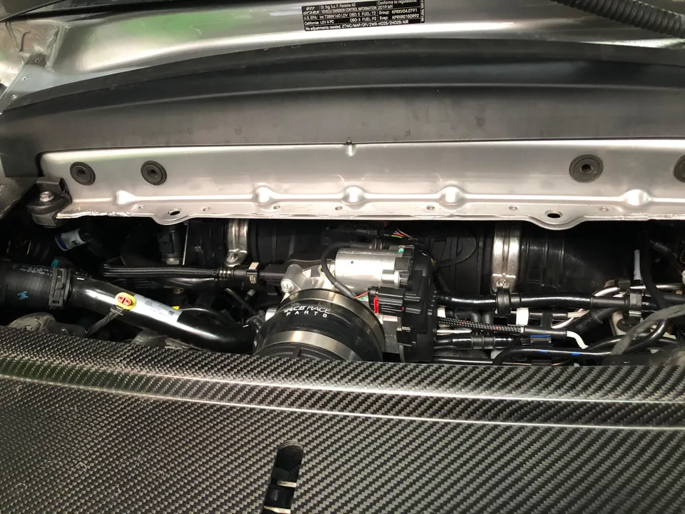 A close-up view of a Porsche engine bay featuring an aftermarket induction system and carbon fiber trim.