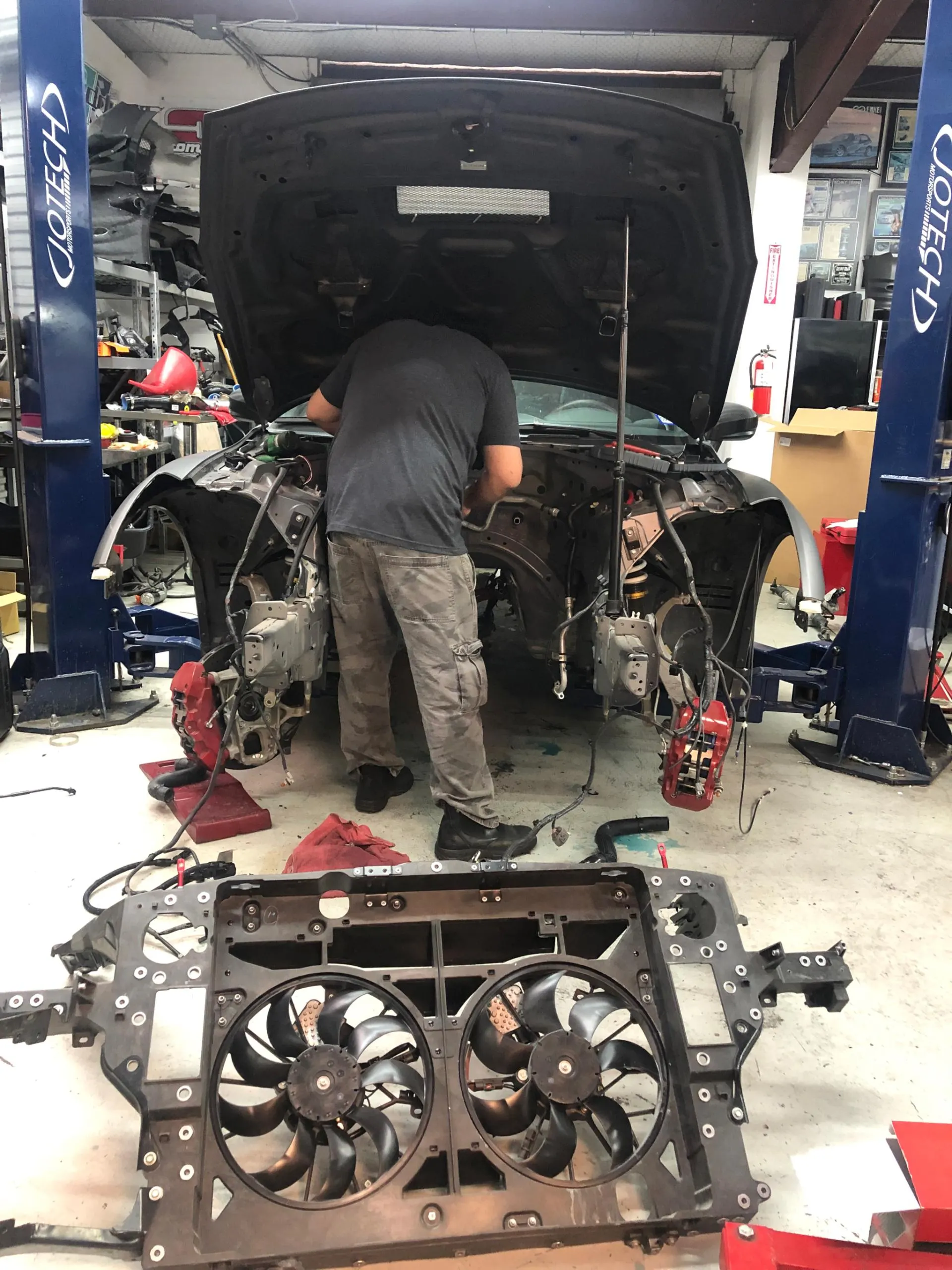 A mechanic works on a disassembled car in a Jotech Motorsports shop, with the front cooling fans removed.