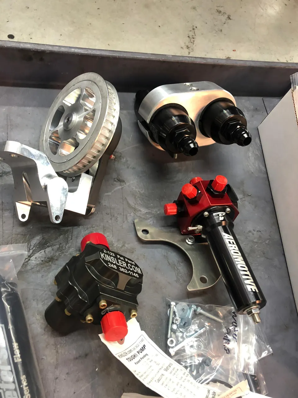 A collection of high-performance fuel system components including Kinsler and Aeromotive fuel pumps on a shop bench.