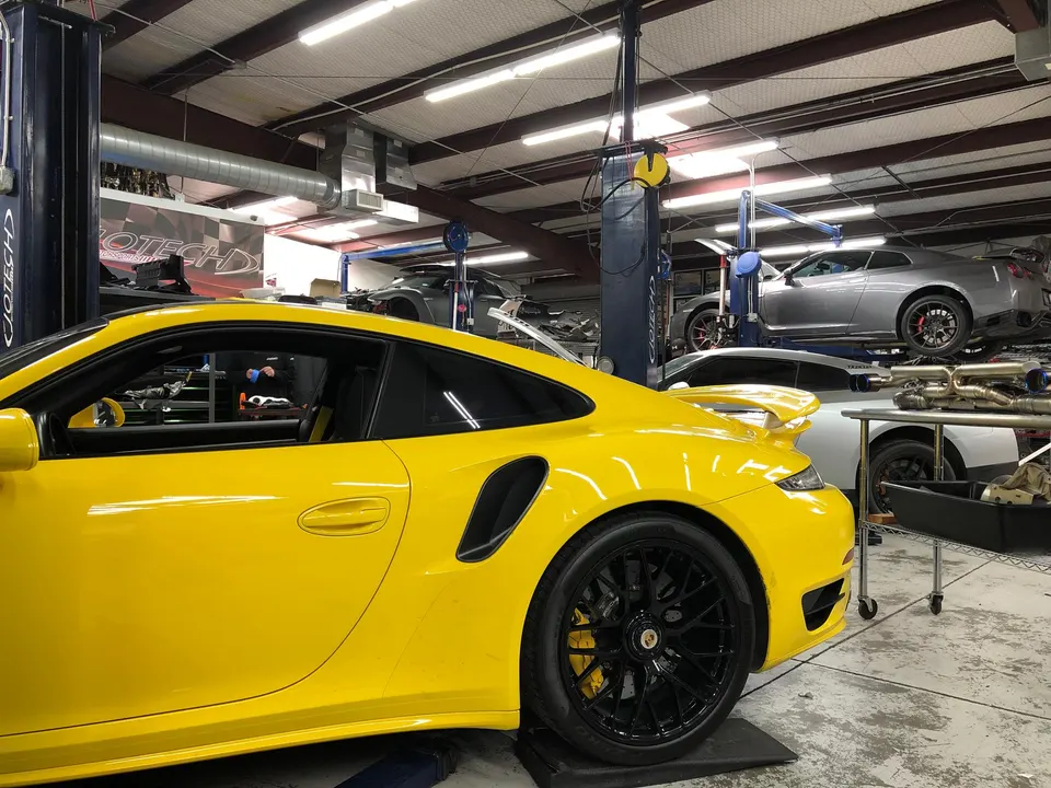 A yellow Porsche and a silver Nissan GT-R on lifts inside a Jotech Motorsports performance tuning shop.