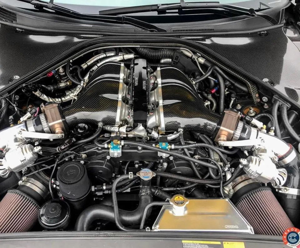 A detailed view of a highly modified Nissan GT-R engine bay featuring a carbon fiber intake manifold, aftermarket air filters, and blow-off valves.
