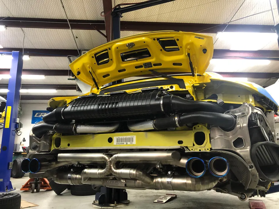 Yellow Porsche 911 on a lift in a shop, showcasing its aftermarket exhaust and induction systems.