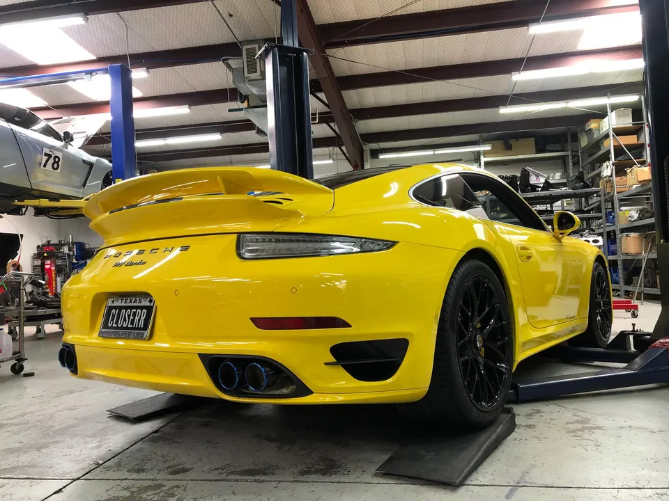 Yellow Porsche 911 Turbo on a lift in a performance shop, showcasing its aftermarket exhaust system.