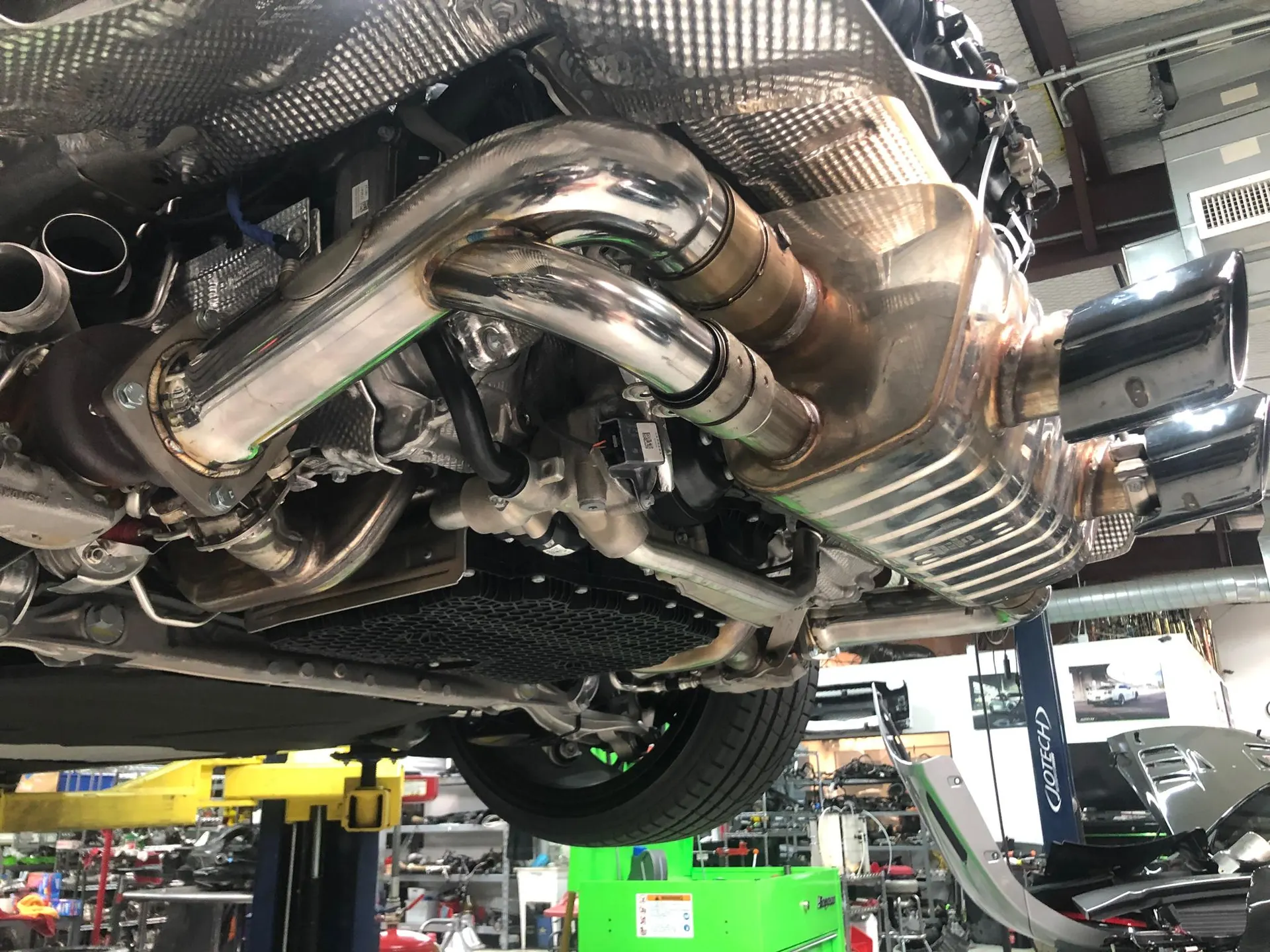 Underside view of a performance car on a lift, showcasing a custom exhaust system with polished mufflers and piping.