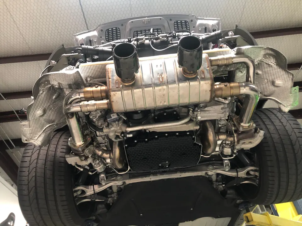 Underside view of a performance car on a lift, showcasing the exhaust system, rear suspension, and drivetrain components.