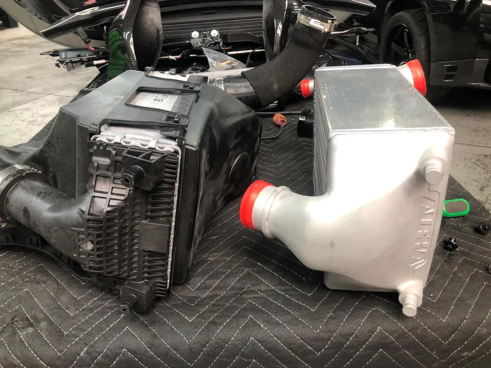 Aftermarket Alpha Performance intercooler next to an OEM intercooler in a performance shop.