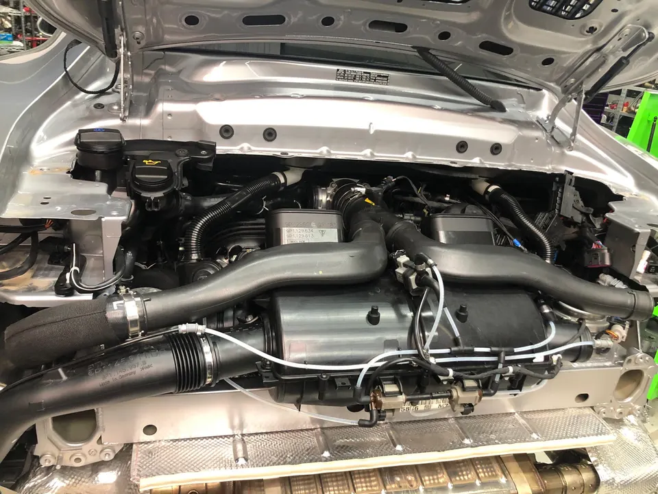 A silver Porsche engine bay with the induction system visible, showing air boxes and piping.