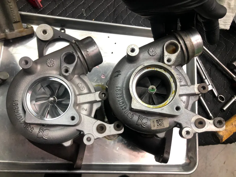 Two turbochargers, one new and one used, on a workbench in a performance tuning shop, ready for installation.