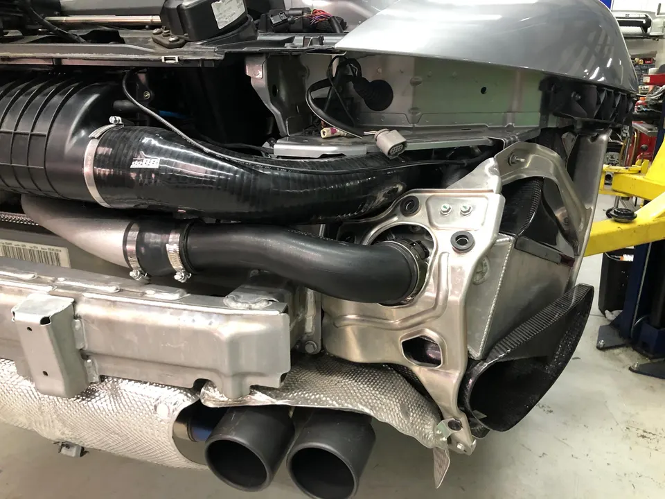 Performance car in shop with rear bumper removed, revealing do88 silicone hoses, intercooler piping, and exhaust tips.