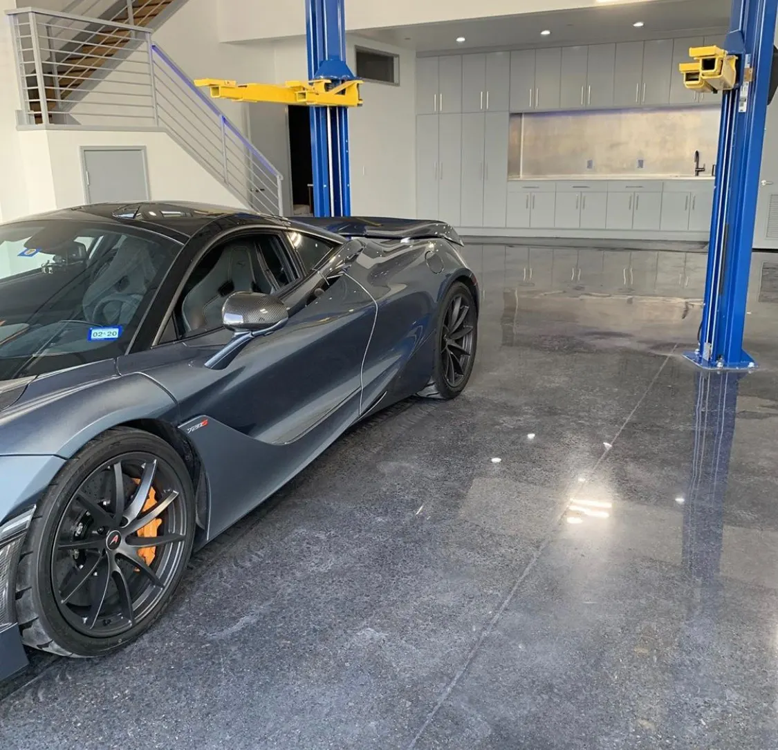 A grey McLaren 720S parked in a clean, modern garage with a blue car lift.