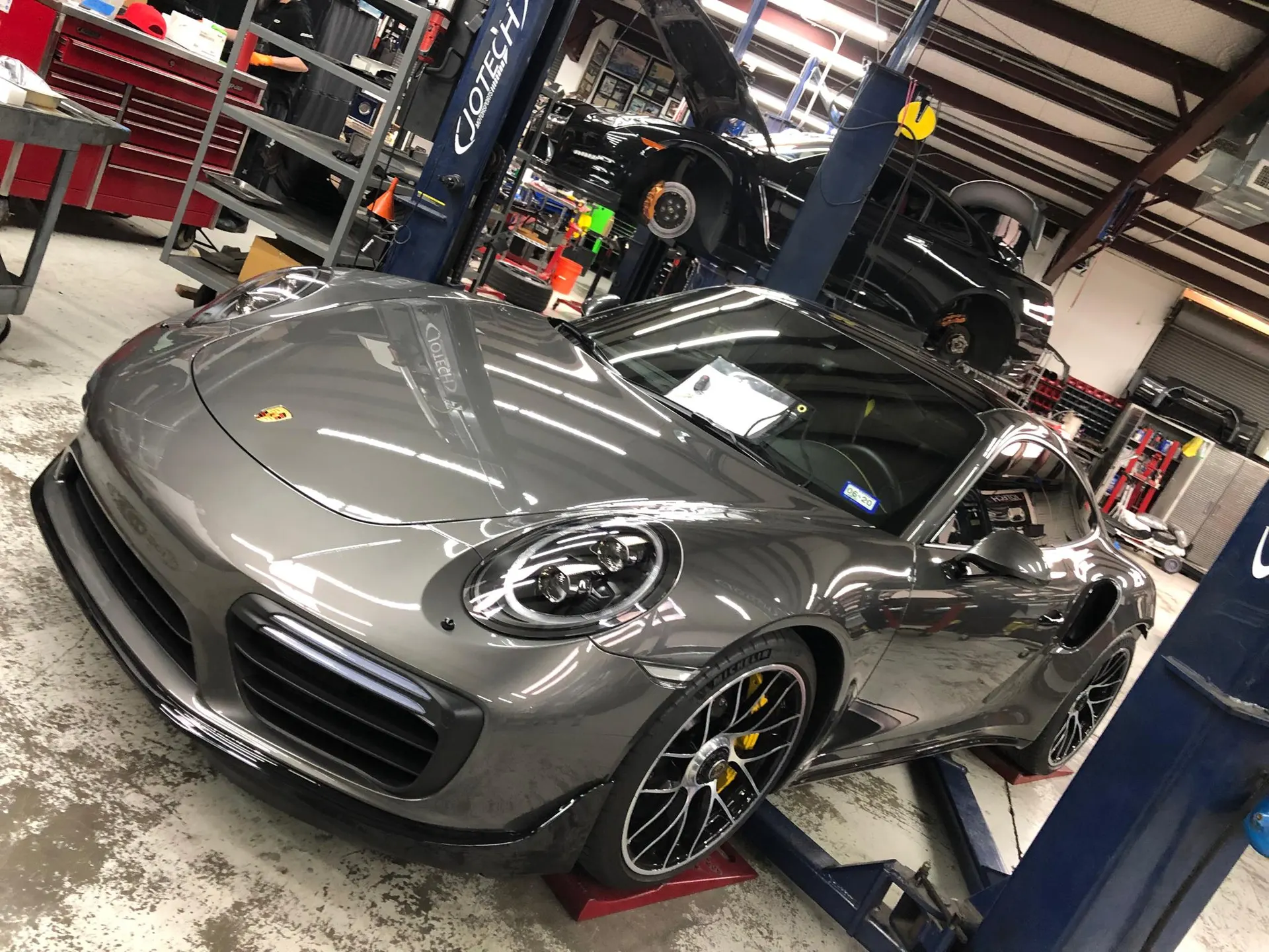 A grey Porsche 911 Turbo S on a lift in a Jotech Motorsports performance tuning shop.