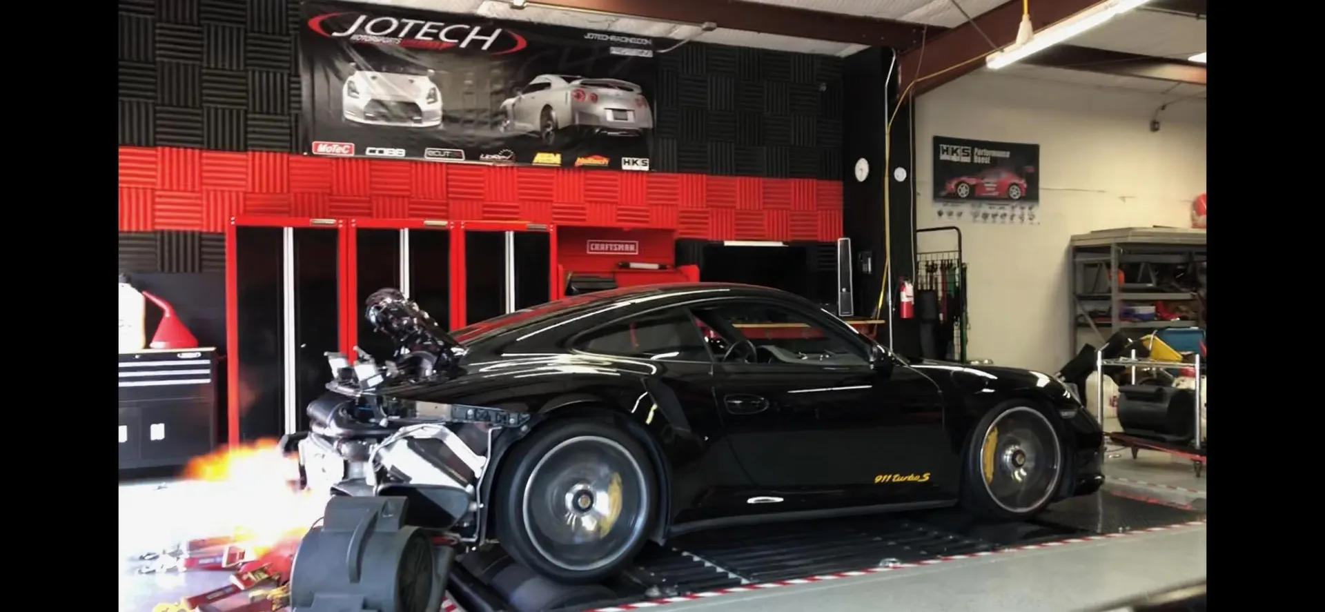 A black Porsche 911 Turbo S on a Jotech Motorsports dyno, shooting flames from the exhaust during a power run.