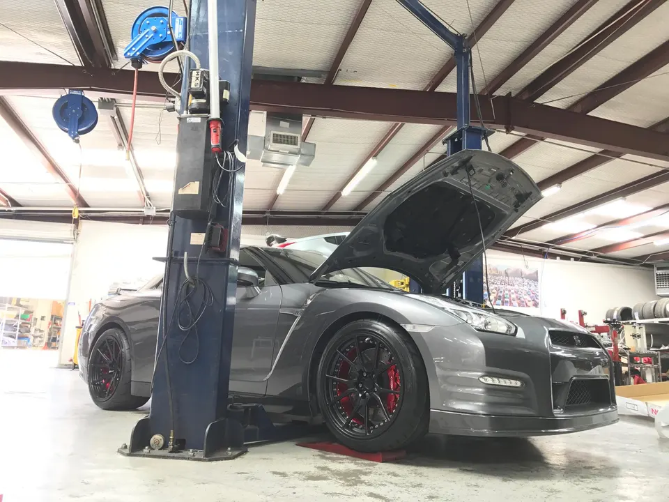 A gray Nissan GT-R with its hood open, on a lift in a performance tuning shop, showcasing aftermarket wheels and red brake calipers.