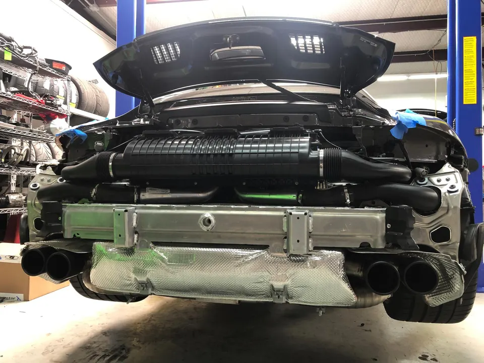 Rear view of a Porsche 911 with its bumper removed, revealing the exhaust system and air intake components in a performance shop.