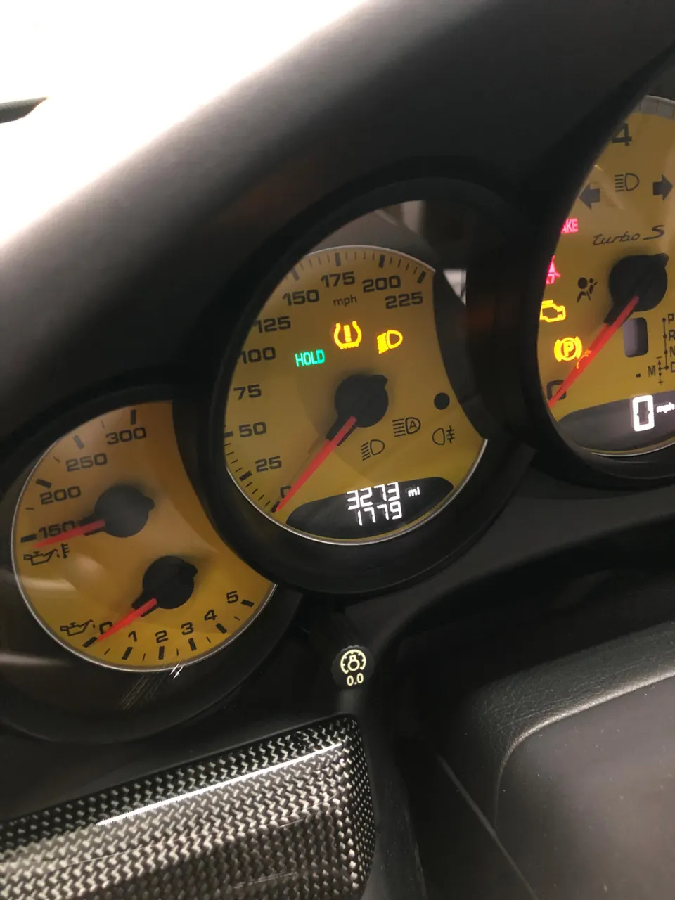 Porsche 911 Turbo S interior detail showing yellow instrument cluster gauges, digital mileage display, and carbon fiber trim.