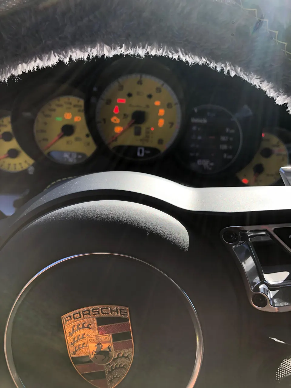 Close-up of a Porsche interior, showing the steering wheel with the Porsche crest and illuminated dashboard gauges.