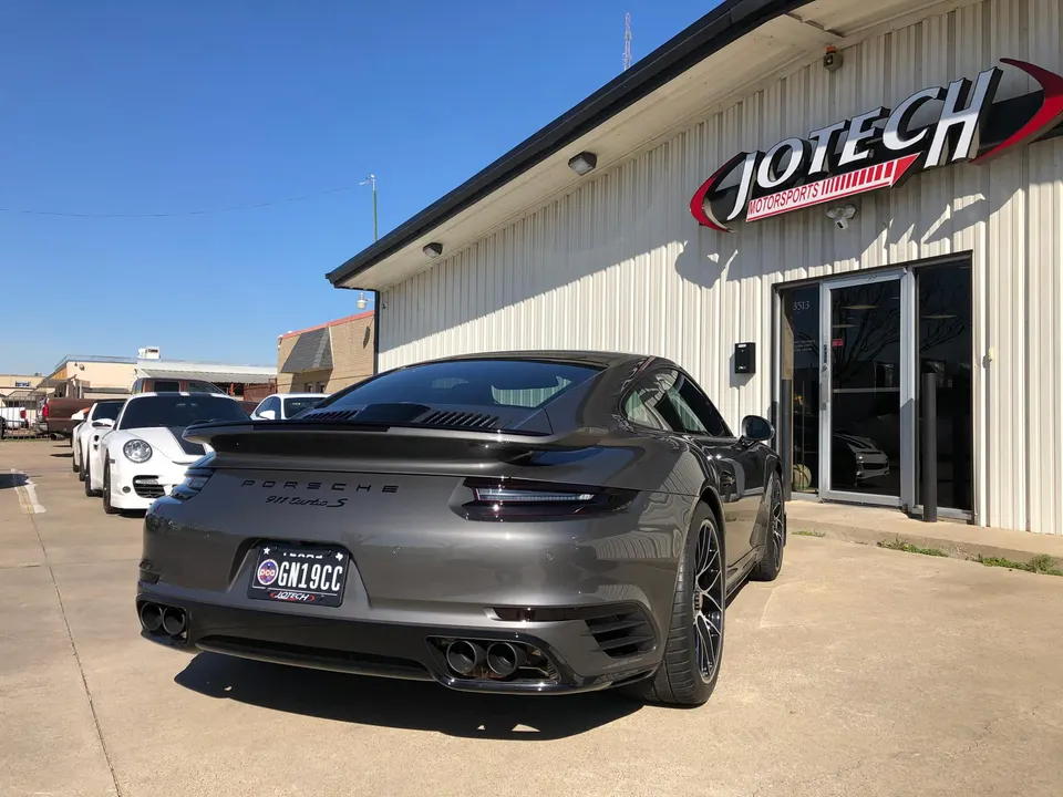 A grey Porsche 911 Turbo S parked outside Jotech Motorsports performance tuning shop.