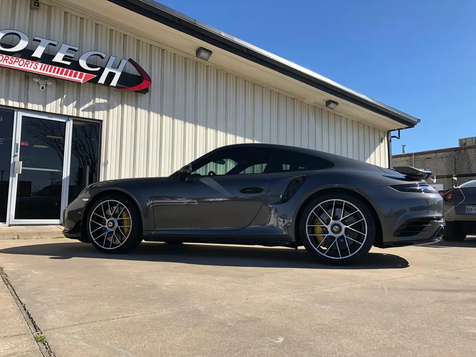 Grey Porsche 911 sports car parked outside Jotech Motorsports shop on a sunny day.