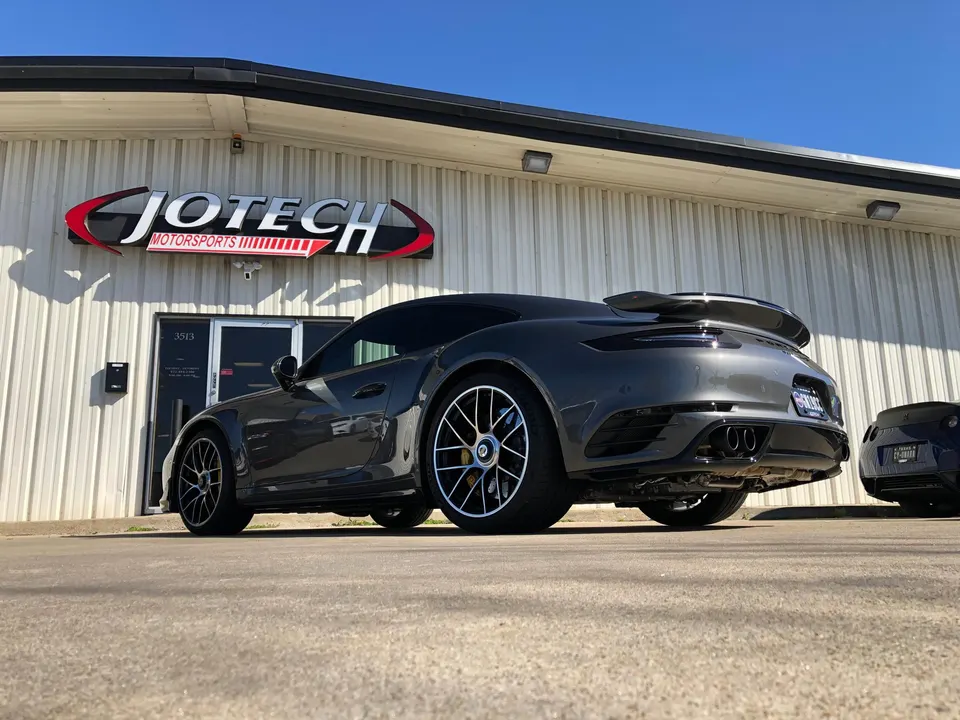 A grey Porsche 911 parked outside the Jotech Motorsports performance tuning shop building on a sunny day.
