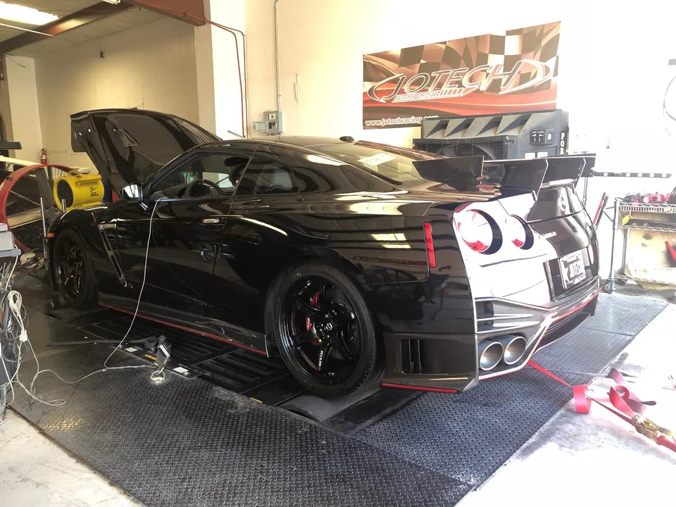 A black Nissan GT-R strapped to a dynamometer at Jotech Motorsports, with its hood open during a tuning session.